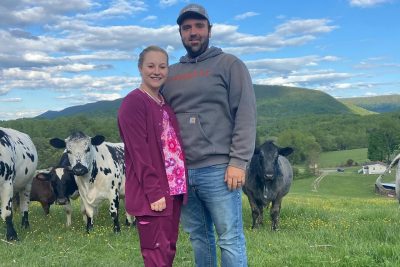 Emily falls standing with another person in a field with cows.