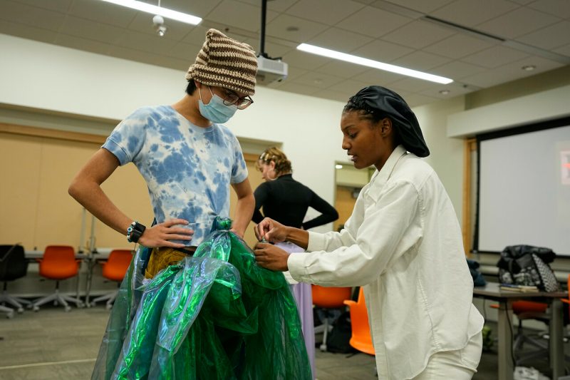 student sews material on second student