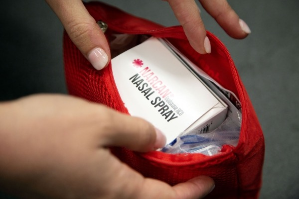 Close-up of a person's hands holding a red bag with a box of naloxone nasal spray inside.