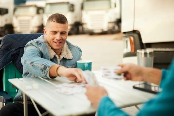 Man casually sitting outside during the day playing cards and drinking coffee.