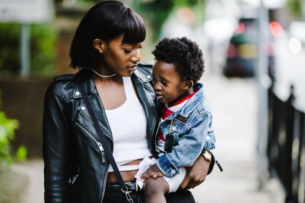 Black woman holding a toddler and walking down a city street.