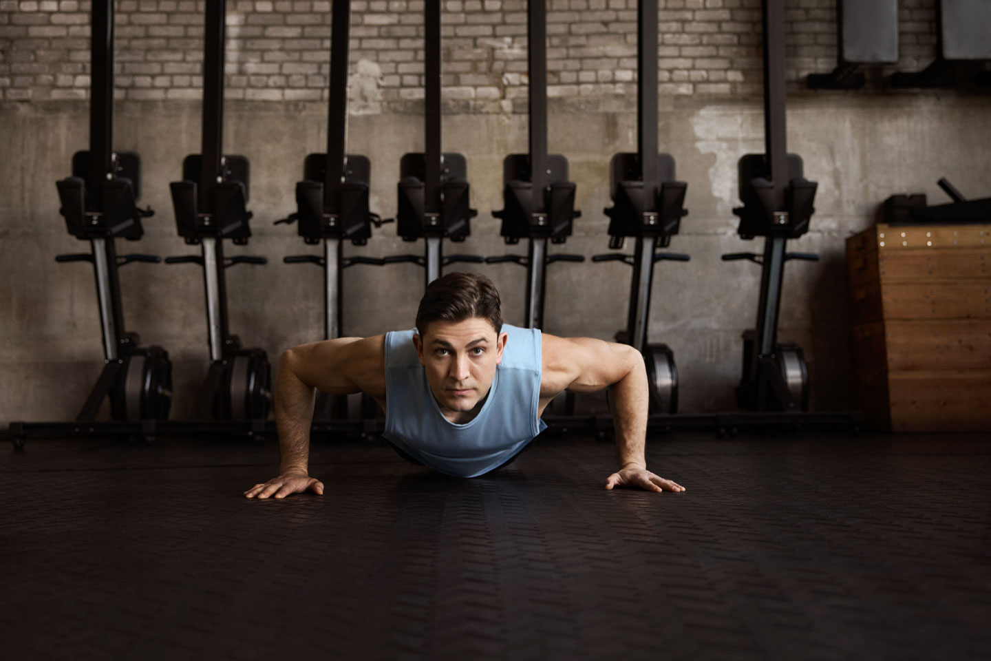 Dr. Jacques H. Hacquebord posing in the middle of a push up on the floor of a gym with weights on a wall behind him