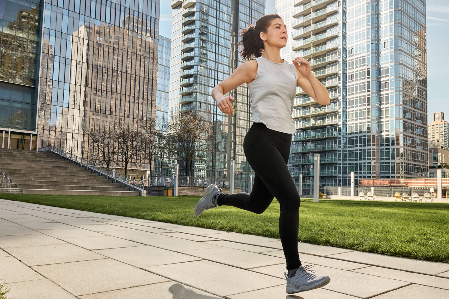 Dr. Mara Karamitopoulos running in the city on a sunny day, with reflective glass buildings behind her