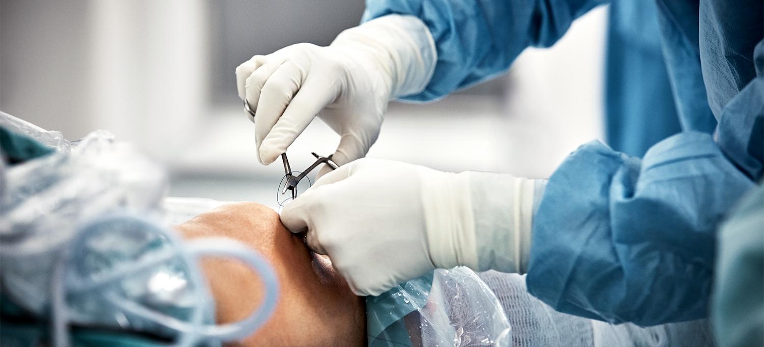 Gloved Hands Placing Sutures in Patient's Knee