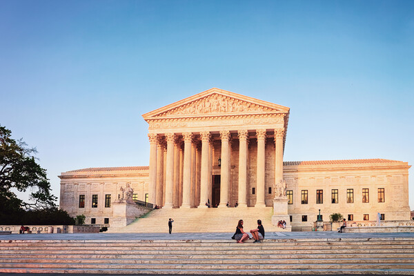 U.S. Supreme Court building with people sitting on the steps and others in the background.