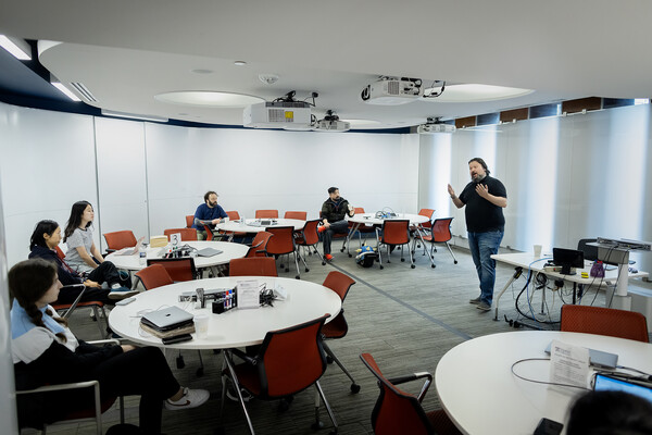 J. Michael Angelis talks to a roomful of students at round tables in Van Pelt Library. 