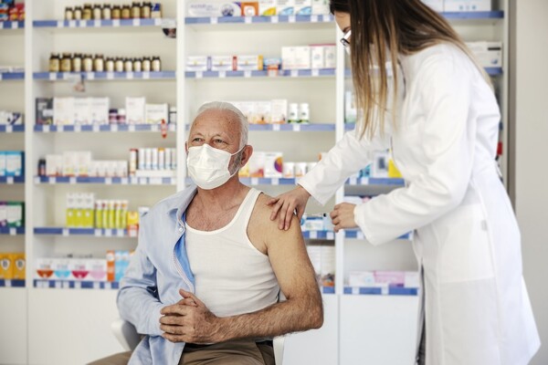 A senior man receives a vaccination from a healthcare provider in a pharmacy,