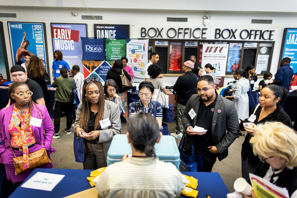 A group of people standing in front of a woman giving out popsicles. In the background, a large sign reading "BOX OFFICE" and advertisements for Annenberg performances. 