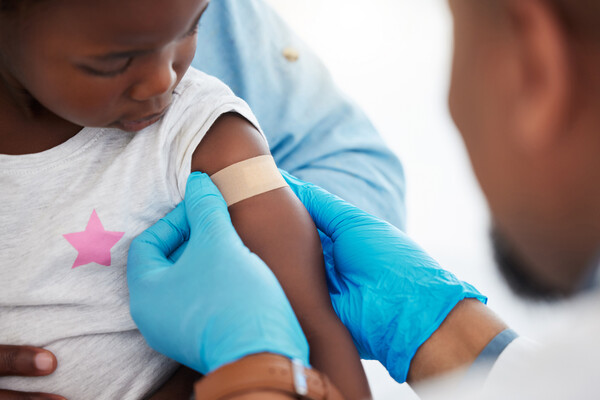 A small child getting a Band-Aid on their arm from a doctor after receiving a vaccine.