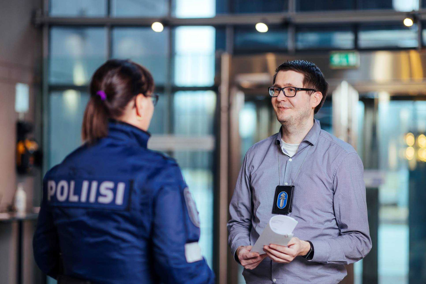 Haalari- ja siviiliasuinen poliisi keskustelevat. Haalariin pukeutunut selkä kameraan. 