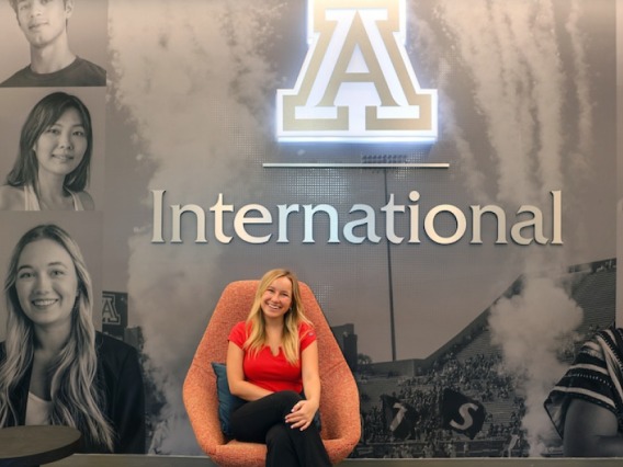 An intern sits in front of a sign for Arizona International