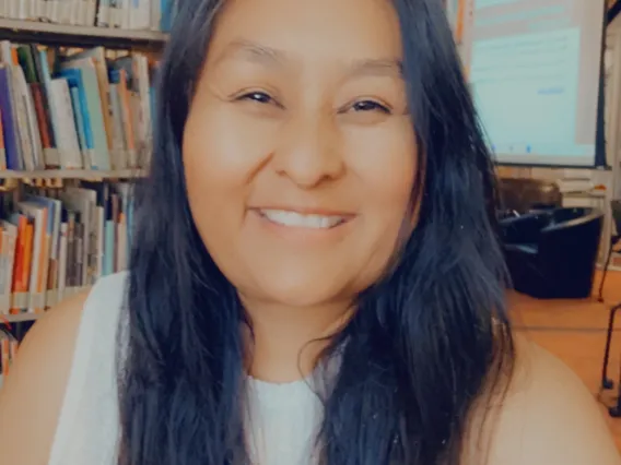 woman with long black hair in front of library bookshelf