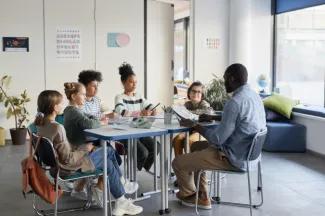 Students listen to teacher at table