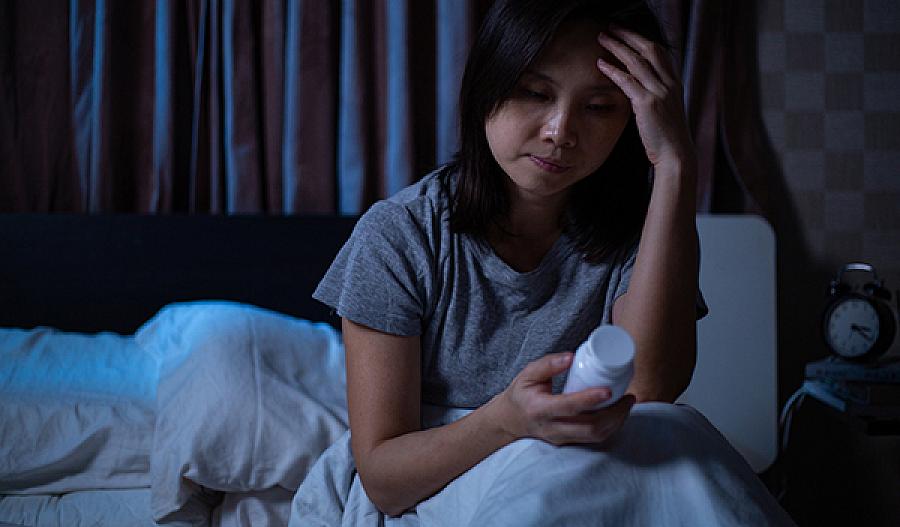 Foto de una mujer sentada en la cama leyendo un frasco de pastillas