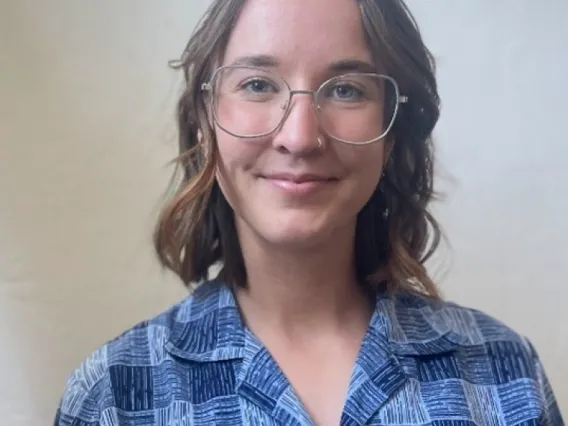 Audrey Beermann, a young person with long brown hair, wearing glasses and a blue flannel shirt