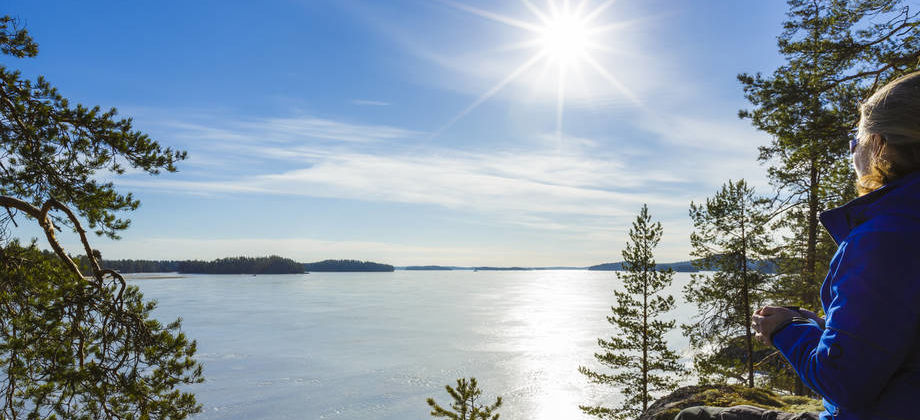 Nainen katselee kalliolla jäiselle järvenselälle.