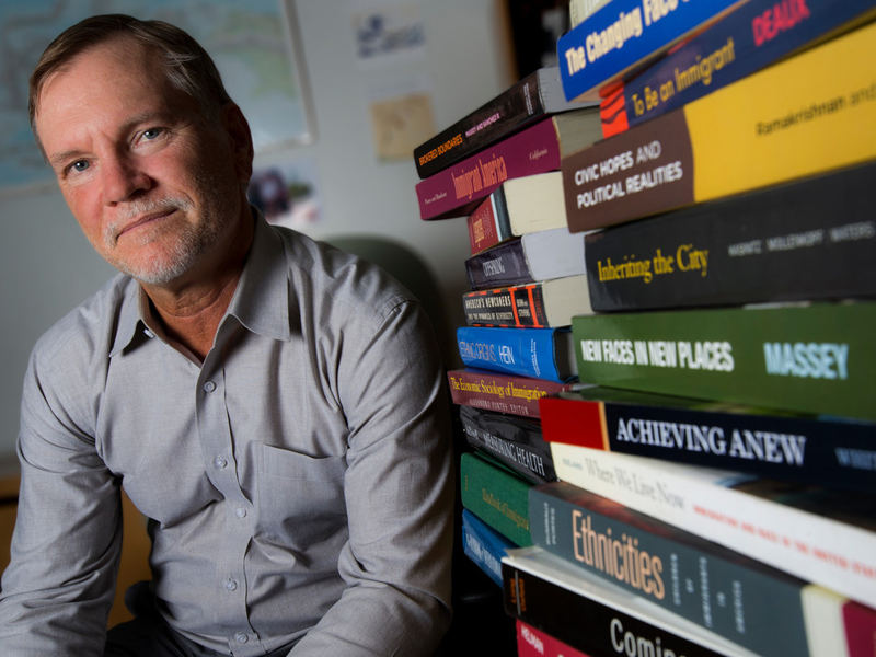 A professor sitting by stacks of books on desk