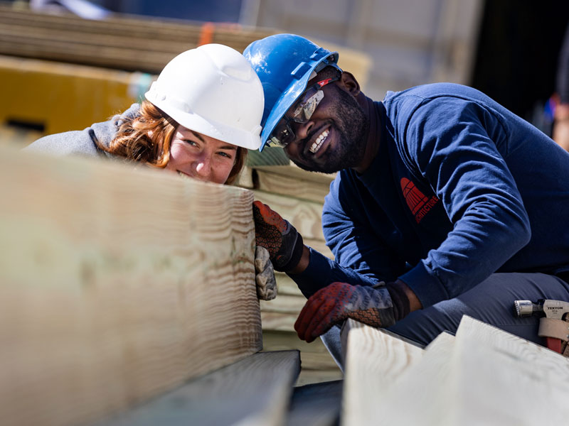 Two students wearing hard hats work at URBAN Build construction site