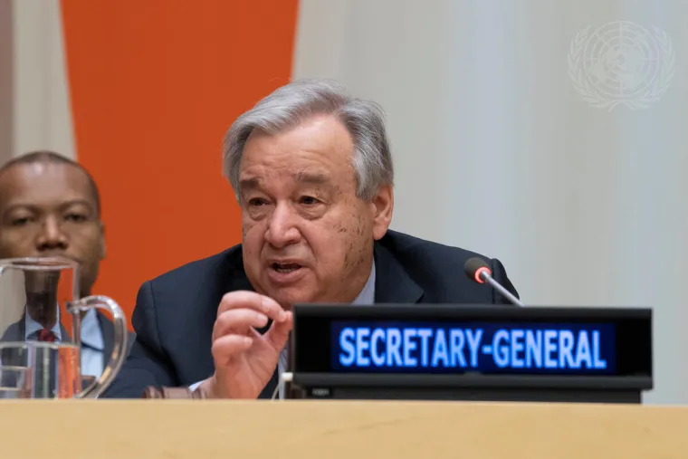 António Guterres speaks from behind an elevated desk with an illuminated tag that reads "Secretary-General" in front of him. 