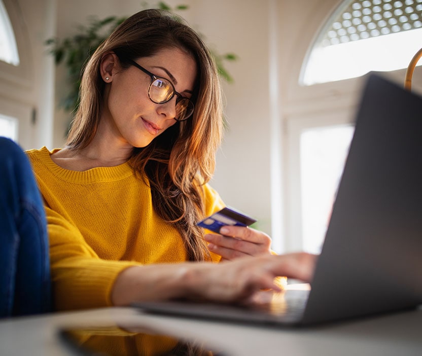 A woman looks at her credit card while using a computer to look up information on Black Friday scams.