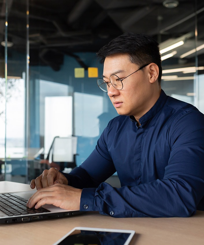 A man wearing glasses concentrates on his laptop, engrossed in his tasks.