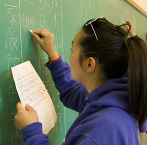 person writing Chinese characters on a chalk board