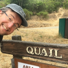 James Quail leaning over a park sign that reads "QUAIL"