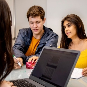 Casal de alunos conversando numa mesa em sala de aula.