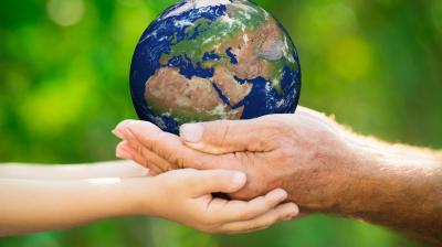 Hands of an elderly person and a child holding a small globe against a blurred green background.