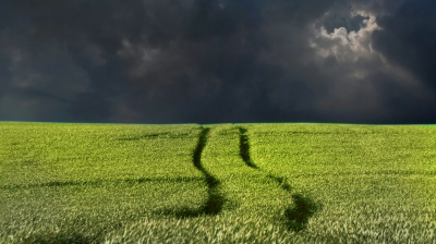 A green field with tire tracks under a dark, stormy sky.