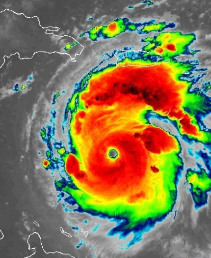 Satellite image of a large, well-defined hurricane with a visible eye, near the Caribbean islands, displaying intense colors indicating varying levels of precipitation and storm intensity.