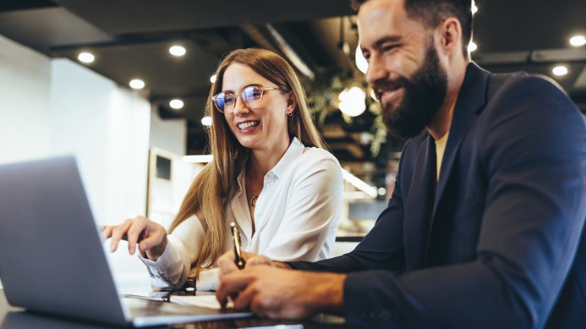 Male and female professionals smiling while looking at laptop