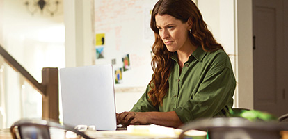 A woman sitting at her kitchen table and looking at appointments on her laptop.