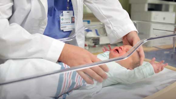 A newborn baby lies in a hospital bassinet cart while being examined by an Erie family medicine resident..