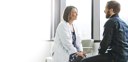 A physician talking to a patient by some windows.