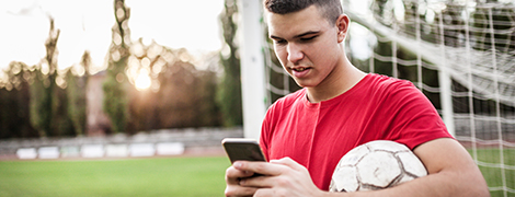 A young man holding a ball under his arm while scheduling an appointment on his phone.