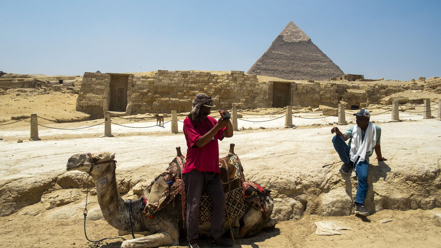 A man checks his mobile phone standing next to his camel while waiting for tourists at the Giza Pyramids Necropolis on the outskirts of Giza on April 30, 2024. (Photo by Jewel SAMAD / AFP) (Photo by JEWEL SAMAD/AFP via Getty Images)