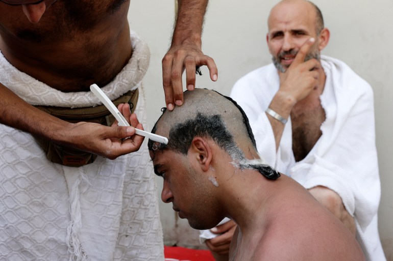 A Muslim pilgrim has his head shaved by another pilgrim holding a straigh razor