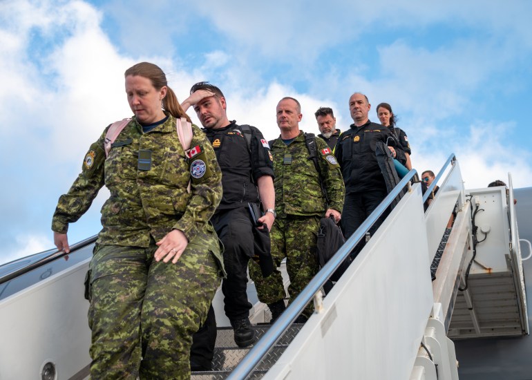 Canadian sailors disembarking after their arrival in Hawaii. A woman is leading the group down a staircase. She's in combat uniform. Others are wearing camouflage and others black uniforms