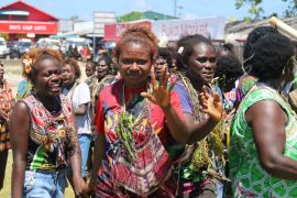 Women prepare to vote in Bougainville's 2019 referendum. They are wearing colourful clothes and gathered together outside a market.