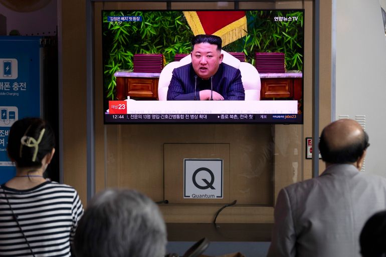 People watching a giant TV screen in Seoul showing a report about North Korea and Kim Jong Un. They are sitting on benches in front of the screen.