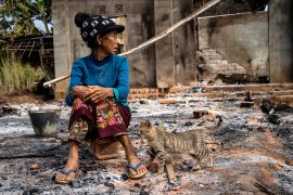 A woman sits outside the rubble of her home after fighting between the military and anti-coup forces in northern Shan state. Her tabby cat is standing next to her.