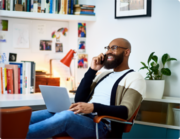 Seated man with laptop smiling while on the phone.