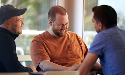 Topher smiling while speaking with two colleagues at a table.