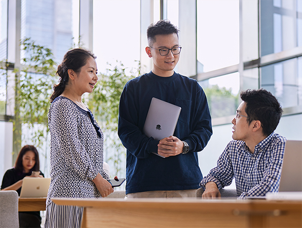 三名 Apple 營運及供應鏈的員工在設有落地玻璃窗的房間內交談。