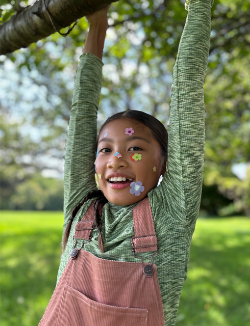 Closeup photo of a girl with flower stickers on her face taken with the iPhone 2x optical-quality Telephoto on iPhone 15