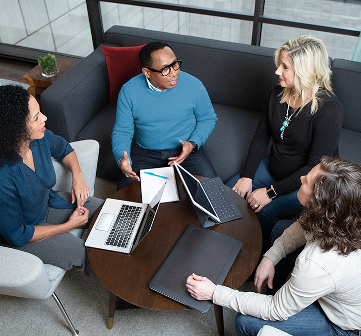 Group of four adults seated together with laptops and legal pads. 