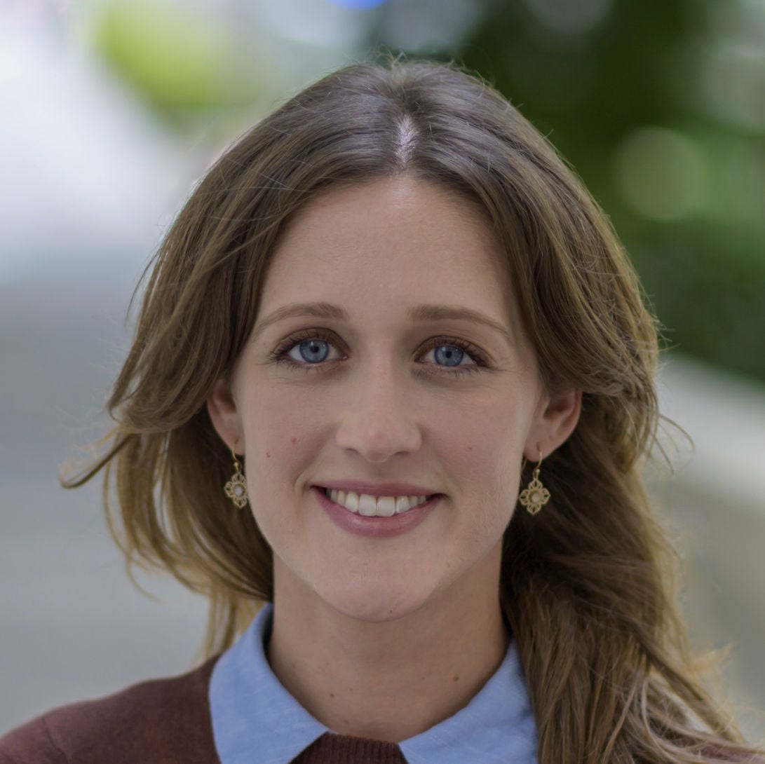 White woman, long brown hair, blue eyes, brown sweater, light blue shirt collar