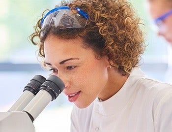 Young female doctor looking into microscope in a lab.