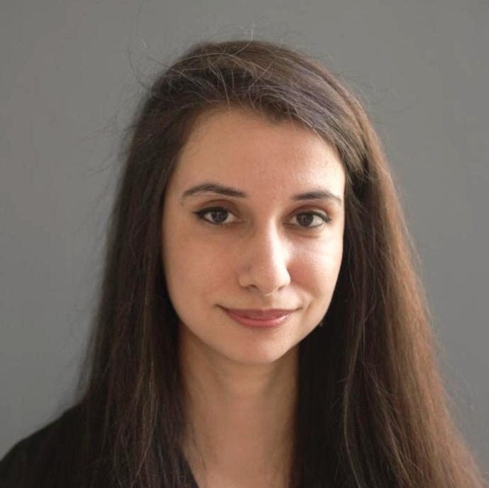 Headshot of Mahera Sohail, long brown hair, dark sweater over a black blouse with orange flecks